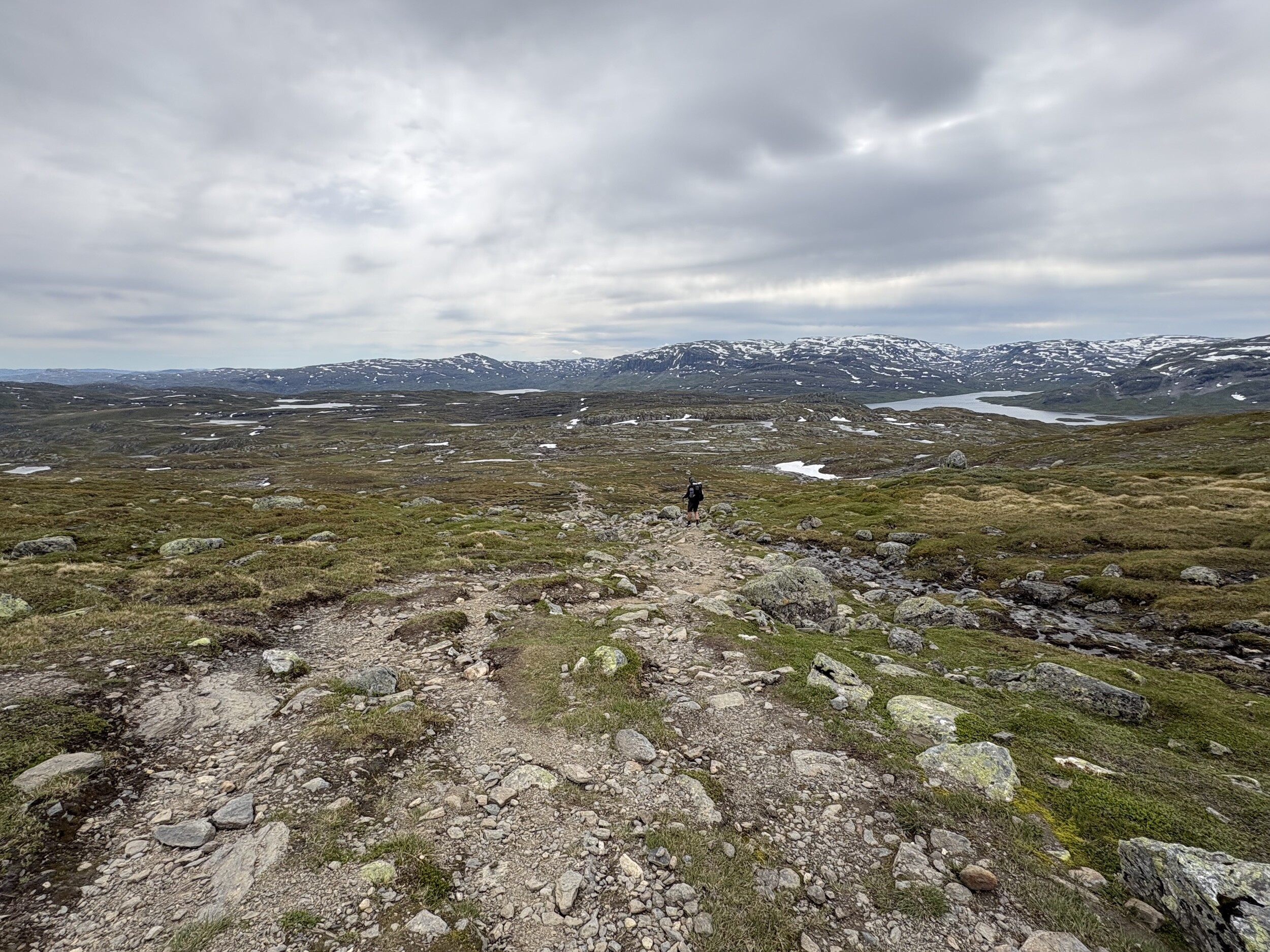 Wir auf steinigem Pfad durch die karge Hardangervidda mit Schnee und Wolken im Hintergrund